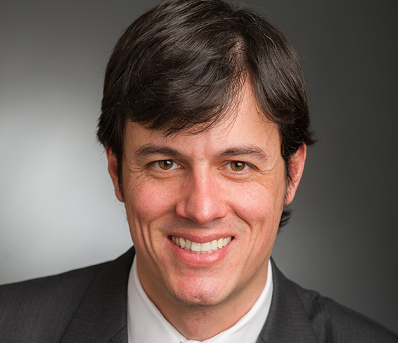 Portrait of a smiling researcher in a suit against a gray background.
